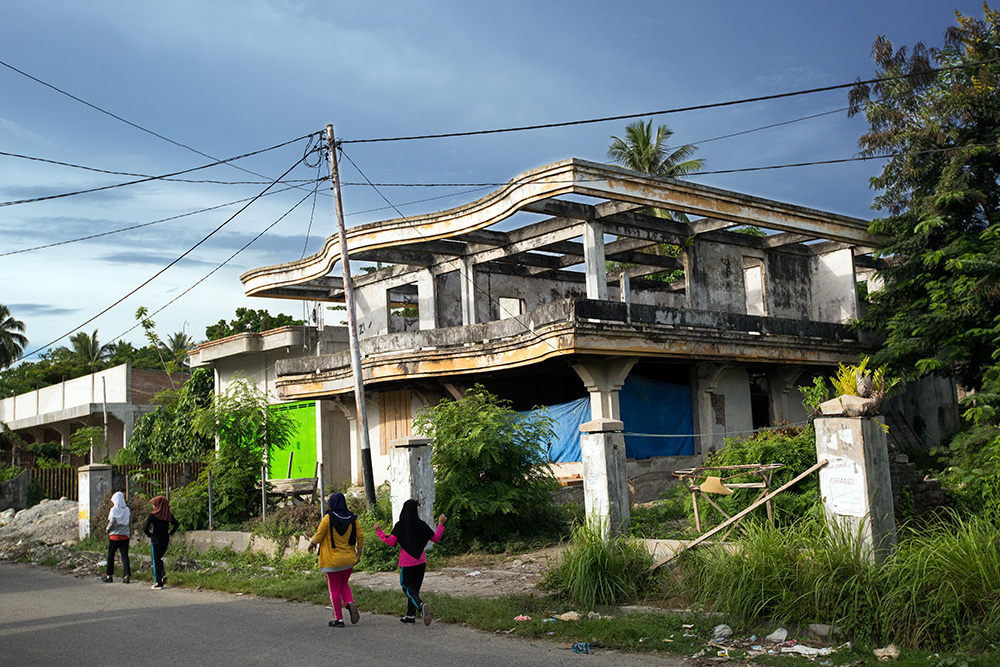 Poso. Muslim teenage girls pass by an abandoned and burned Christian family's house.