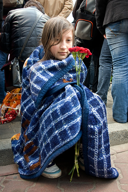 The girl sits among people at Piłsudski Square.