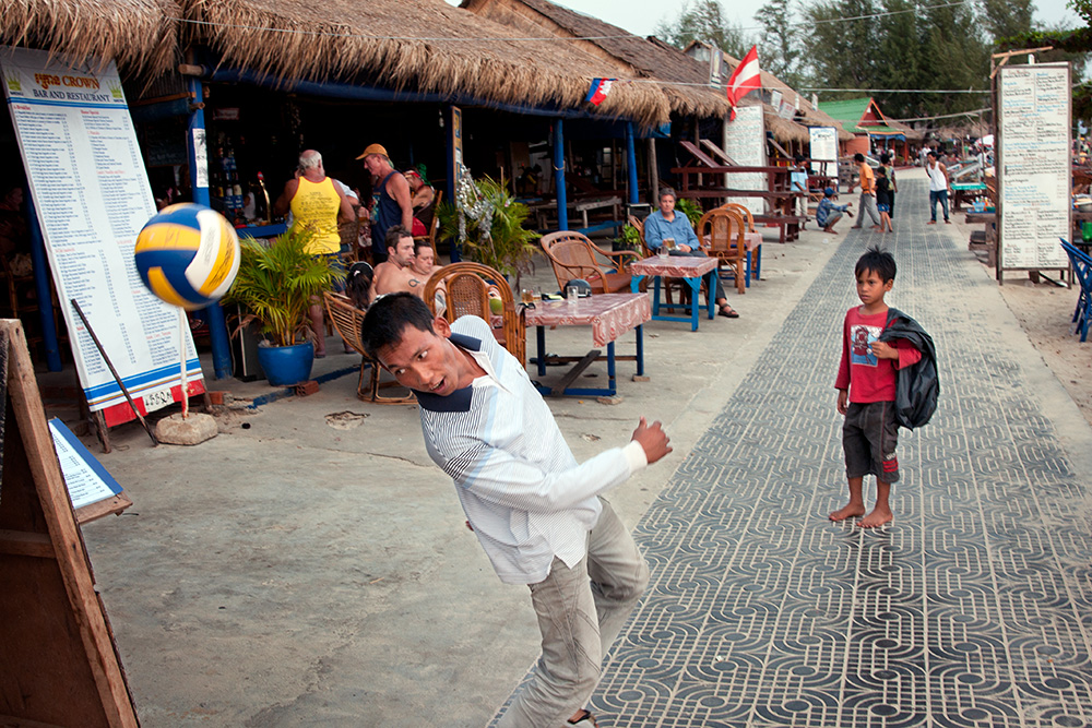 A young scavenger watch a man playing a ball. Seafront promenade in Sihanoukville, a popular tourist destination in Cambodia.