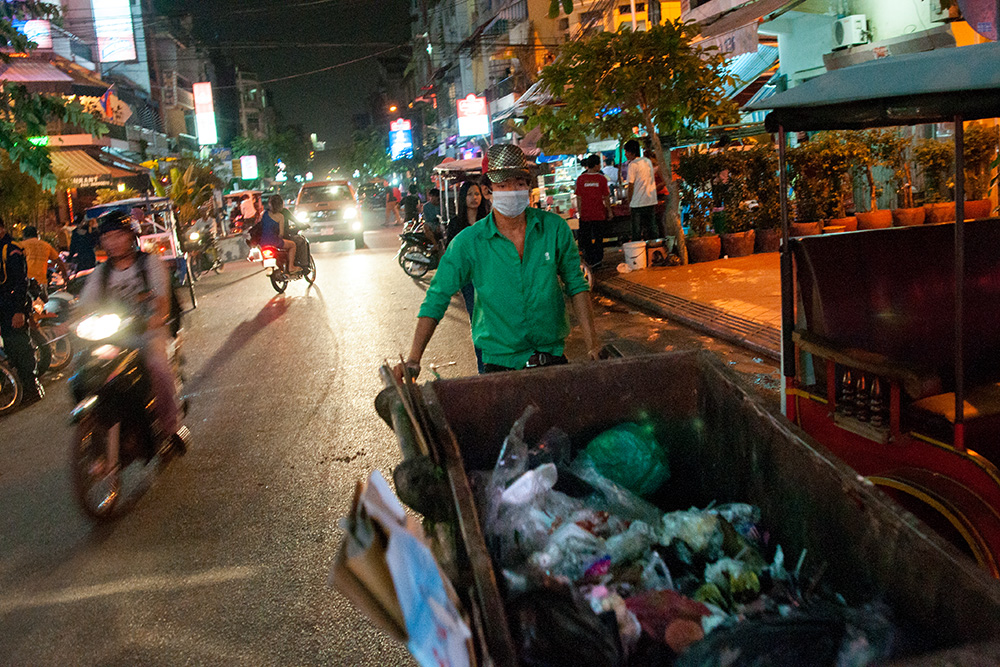 A cleaning company's employee carries garbage container at night in center of Phnom Penh. All potentially valuable materials whose can be sold are already taken away by scavengers.